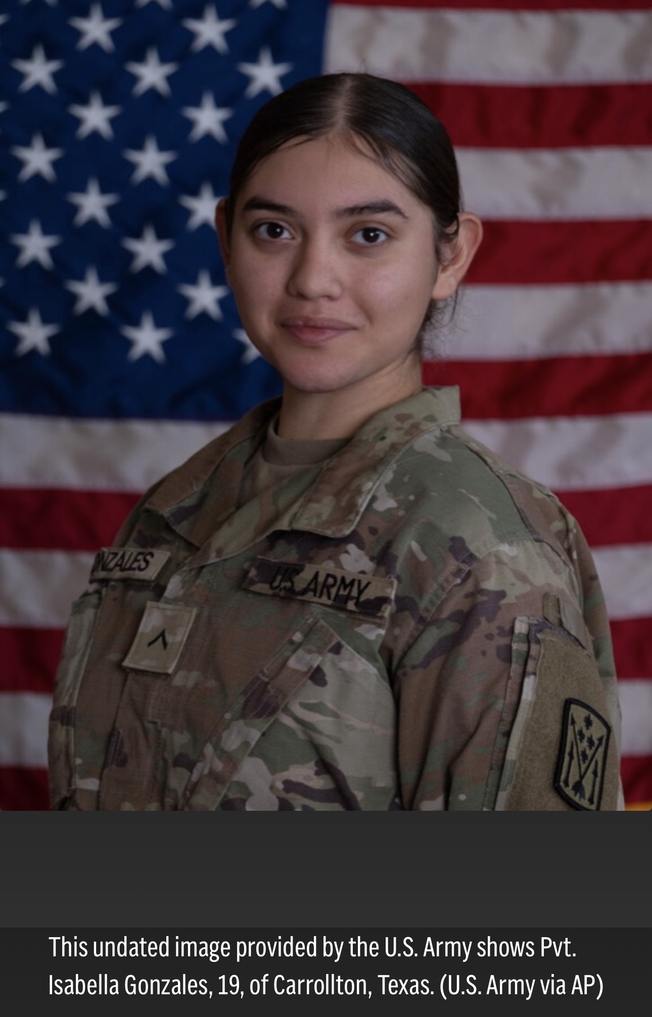 An official US Army portrait of Private Isabella Gonzales, of Carrollton, TX. She is a young woman with light brown skin and wide-set eyes, looking directly into the camera with a slight smile on her face. She is wearing camo fatigues. Behind her is an American flag. She died this week in Jordan.